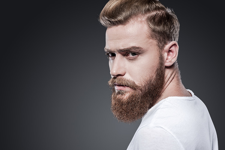 Confident in his look. Thoughtful young bearded man looking over shoulder while standing against grey background